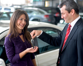 A new vehicle buyer gets her keys from her auto dealership representative after buying a new car.