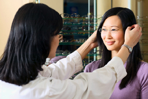 An optician fits a vision appointment patient for new prescription eyeglasses after her eye exam.