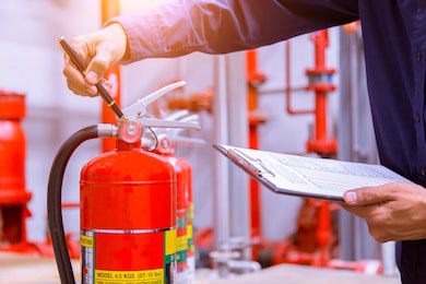 A fire protection technician checks the pressure on a fire extinguisher as part of a fire readiness plan.