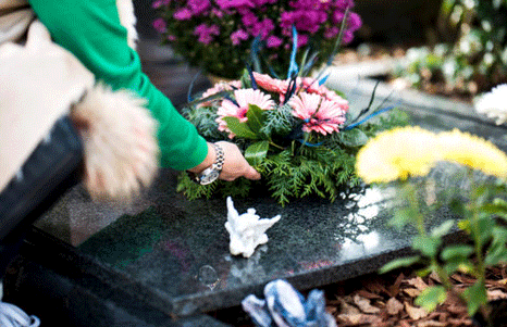A woman leaves flowers at the gravestone of a loved one in a local cemetery after funeral services and burial.