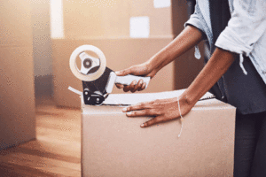 A residential moving customer packs belongings in a moving box and tapes it shut before it gets loaded to the moving truck for an interstate move.