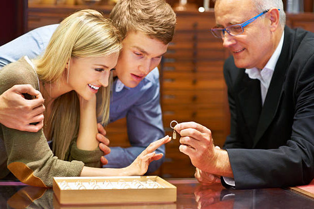 A local jeweler helps a young couple who is engagement ring shopping with ring sizing services.