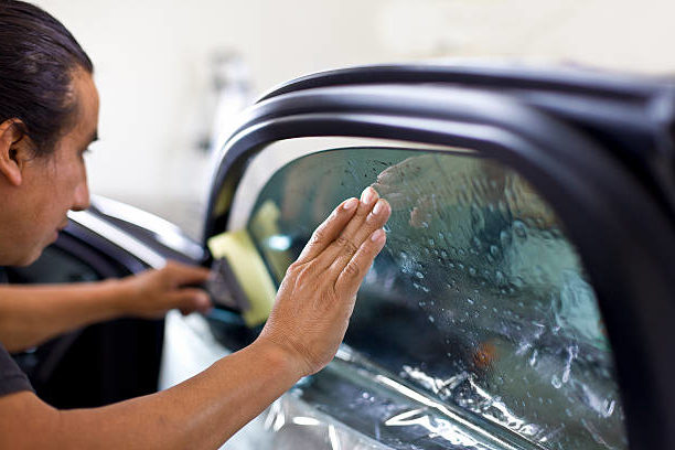 A technician installs dark tint on a front car window at a local auto glass tinting shop.