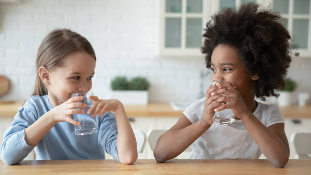 Two little girls sit at a kitchen table and drink fresh, clean water from their home water filtration system installed and maintained by a local water treatment company.