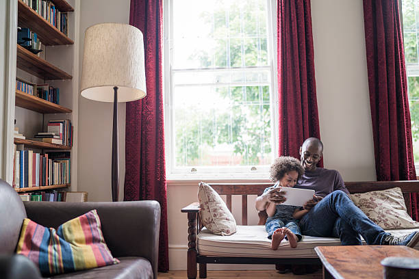 A father and daughter read in front of their new curtains and window treatments that help their house feel like a home.